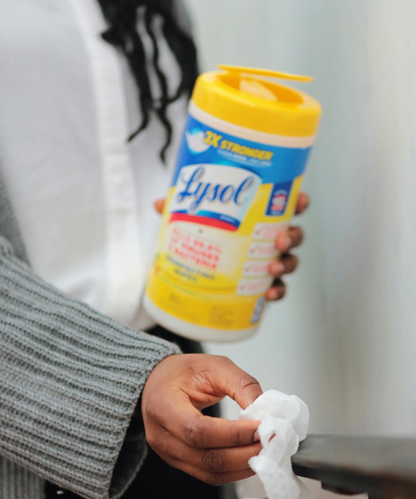 A hand holding a tub of disinfecting wipes